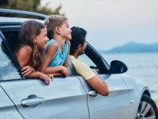 Famille souriante dans une voiture grise garée devant la mer