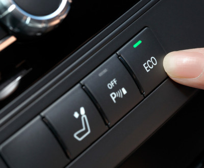 Doigt appuyant sur un bouton de commande de voiture, avec des icônes liées à l'éco-conduite sur le tableau de bord