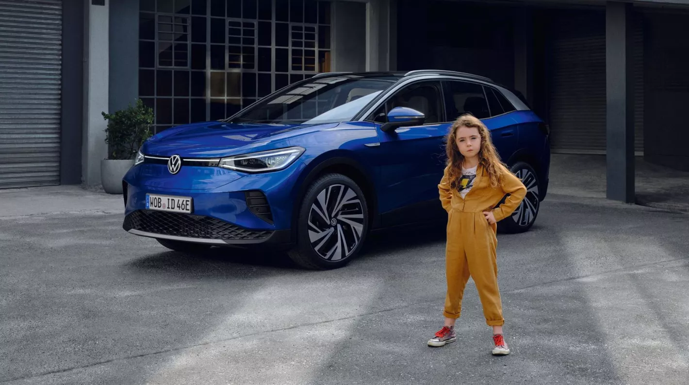 Femme en combinaison jaune posant à côté d'une voiture bleue moderne