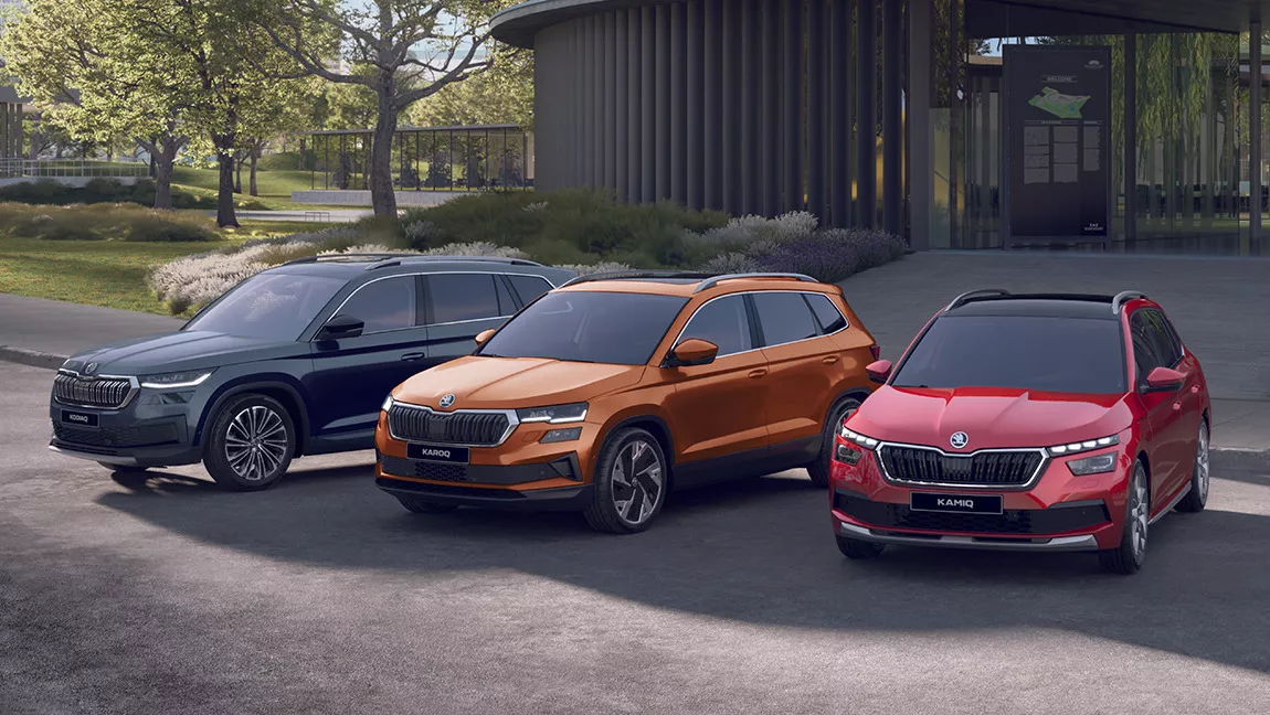 Trois voitures SUV Skoda noire, orange et rouge devant un bâtiment en verre