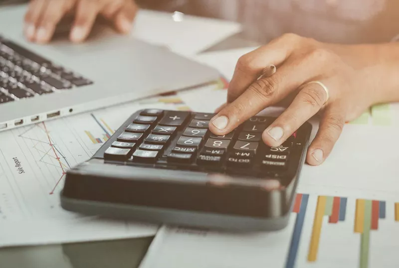 Un professionnel travaillant méticuleusement sur son ordinateur portable tout en utilisant une calculatrice