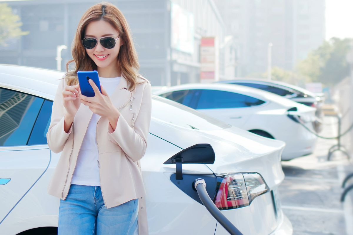 Femme élégante avec son téléphone près d'une station de recharge pour sa voiture électrique