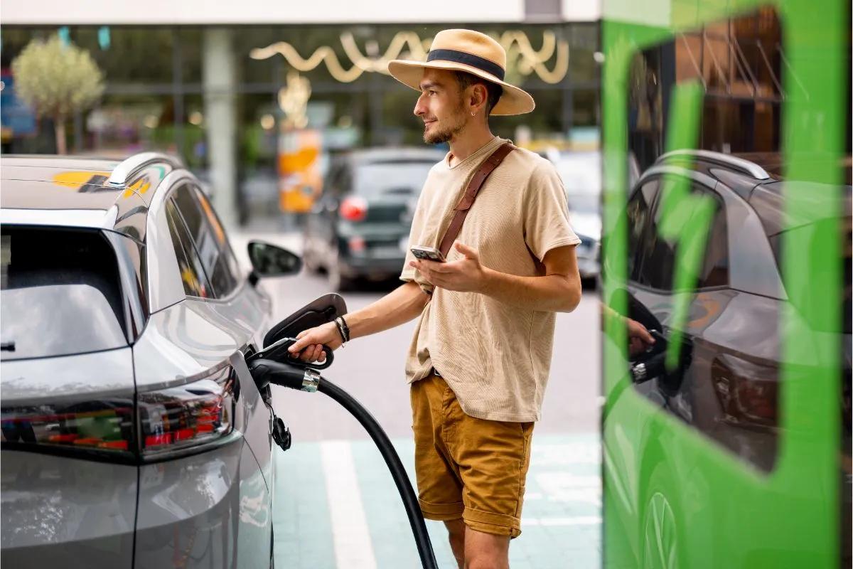 Homme habillé de manière détendue en train de recharger sa voiture électrique sur une borne publique pendant son trajet de vacances